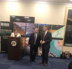Three people stand during a presentation with a congressional podium featured. 